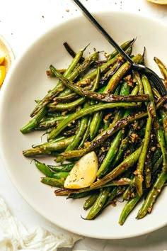 a white plate topped with asparagus covered in seasoning next to lemon wedges