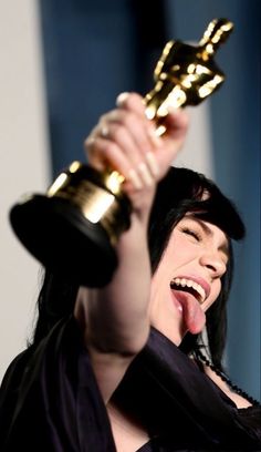 a woman holding an award up in the air with her mouth open and tongue out