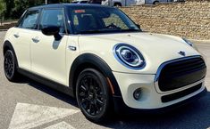 a white mini cooper parked in a parking lot next to a brick wall and trees