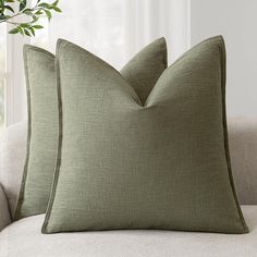 two green pillows sitting on top of a white couch next to a potted plant