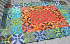 a multicolored patchwork quilt on a wooden deck in the sun with shadows