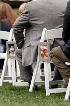 two men in suits are sitting on white folding chairs with their backs turned towards the camera