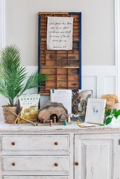 a white dresser topped with lots of clutter next to a wooden wall hanging on the wall