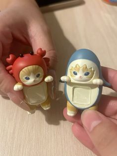 two small toy dolls are being held by someone's hand on a table top