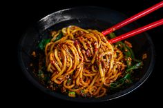 some noodles are in a black bowl with red chopsticks