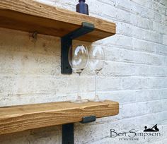 two wine glasses are sitting on a shelf next to a bottle and glass holder in front of a white brick wall