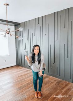 a woman standing in an empty room with wood flooring and walls painted gray, holding up her phone