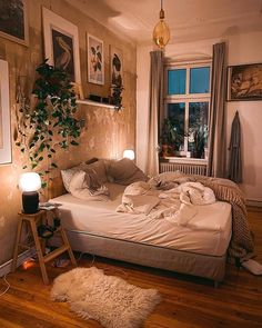 an unmade bed sitting in a bedroom next to a window with plants on it