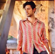 a man standing under a wooden structure with his hands in his pockets and looking at the camera