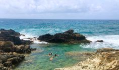 two people swimming in the ocean next to some rocks and water on a sunny day