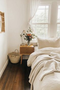 a bed with white sheets and pillows in a bedroom next to a window filled with plants