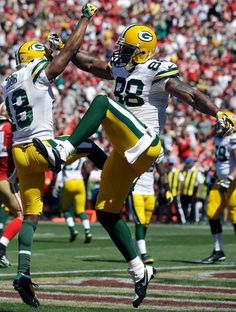 two green bay packers are jumping in the air to catch a football during a game