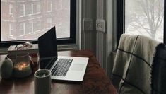 an open laptop computer sitting on top of a wooden desk next to a cup and candle