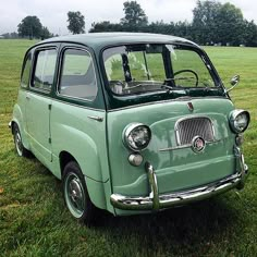 an old green car is parked in the grass