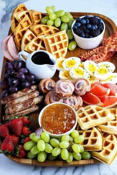 a wooden platter filled with waffles, fruit, and other food items