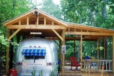 an airstream sits in the middle of a wooded area with picnic tables and chairs