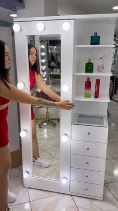 a woman standing in front of a white vanity mirror with lights on it's sides