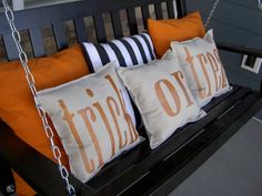 three orange and white pillows on a black porch swing