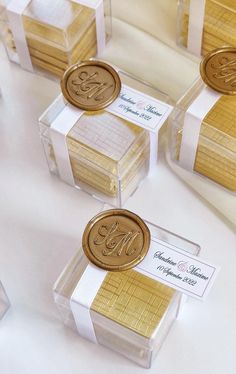 four clear boxes with gold foiled monogrammed labels on them are sitting next to each other