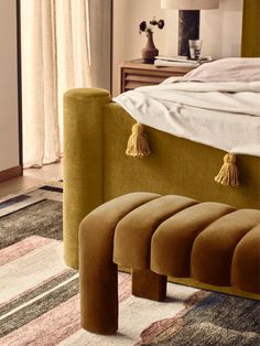 an upholstered bed with tasseled foot stools in the foreground