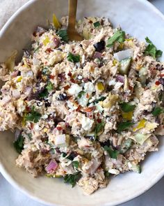 a white bowl filled with chicken salad on top of a table next to a wooden spoon