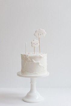 a white cake sitting on top of a white table next to a cupcake with candles in it