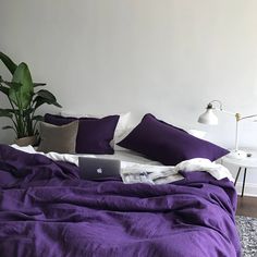 a laptop computer sitting on top of a purple comforter in a room with white walls