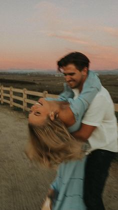 a man holding a woman on his back in front of a wooden fence at sunset