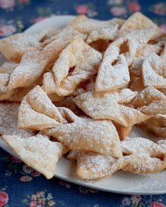 a white plate topped with lots of powdered sugar covered pastries on top of a wooden table