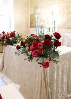 red roses and greenery are arranged on the table