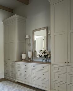 a large white dresser sitting next to a mirror and vase with flowers on top of it