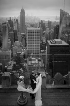 a bride and groom standing on top of a building with the city in the background