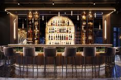 a bar with several stools and bottles on the wall behind it in a dimly lit room