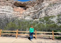 a woman standing at the top of a hill looking over a wooden fence with a cliff in the background