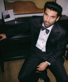 a man in a tuxedo sitting next to a piano and looking at the camera