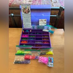 a purple box filled with lots of different colored beads and plastic containers on top of a wooden table