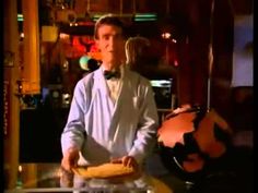 a man standing in front of a table with food on it and an orange vase behind him