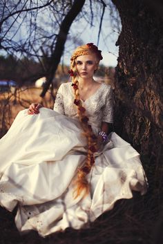 a woman in a white dress sitting under a tree with her long hair curled up