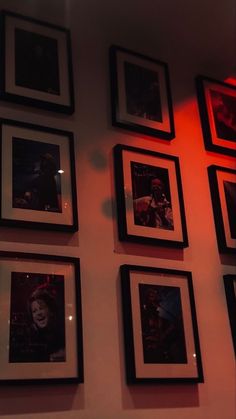 a wall with many framed pictures on it and a red light shining through the window