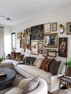 a woman sitting on top of a couch in front of a wall filled with pictures