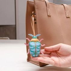 a hand holding a small toy in front of a purse