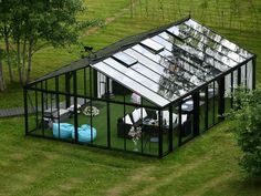 an aerial view of a glass house in the middle of a grassy area with chairs and tables