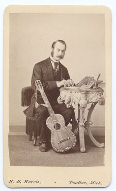 an old black and white photo of a man with a guitar sitting on a chair