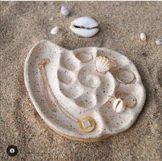 shells and rings are arranged on the sand near an object that looks like a seashell