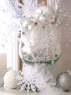 a glass vase filled with white snowflakes and ornaments on top of a mantle