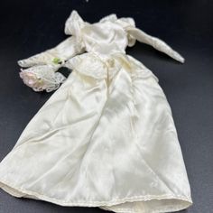 a white dress with flowers on it and a small doll in the back, sitting on a black surface