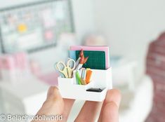 a person holding up a small white box filled with office supplies