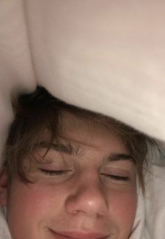 a young boy laying in bed with his eyes closed and head tucked under the covers