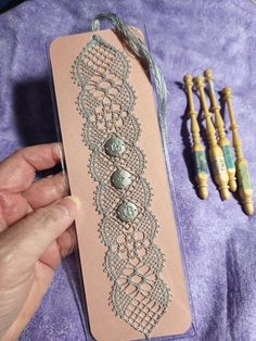 a hand holding a piece of fabric with buttons on it next to some beads and thread