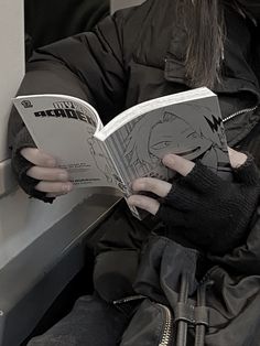 a person sitting down reading a book on a subway car while wearing black gloves and holding an umbrella